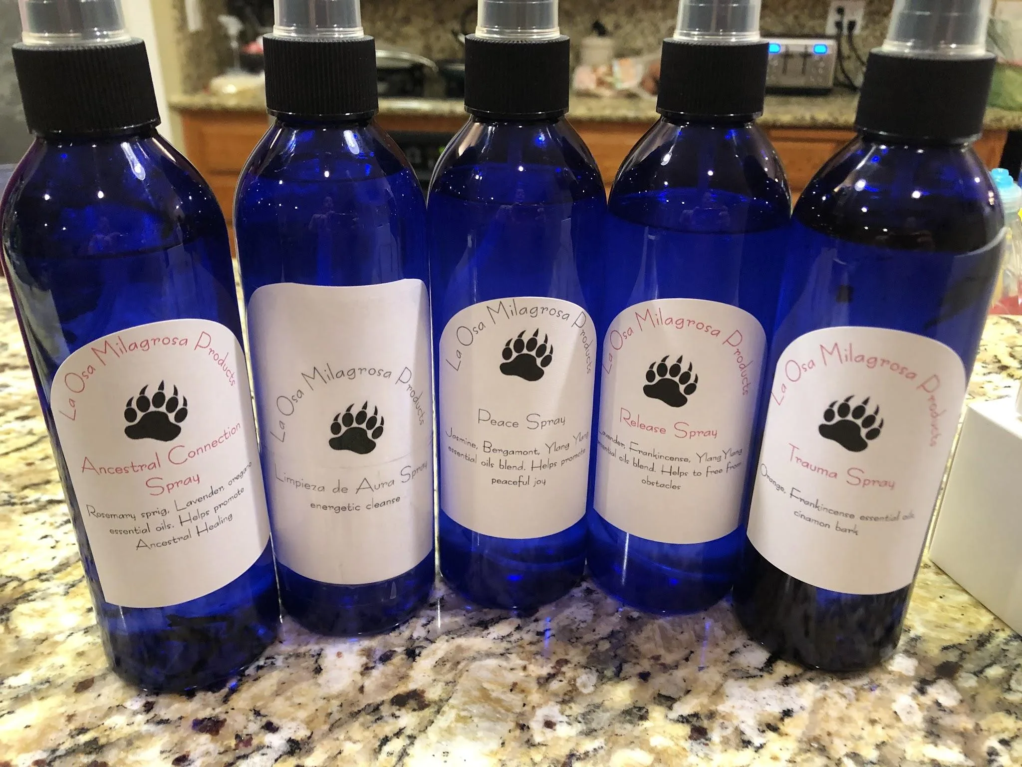 Five blue La Osa Milagrosa Sacred Spray bottles, including Ancestral Connection, Limpieza de Aura, Peace, Release, and Trauma sprays.